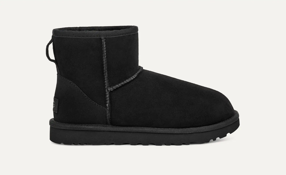 Black UGG boot on a light gray background.UGG Women's Classic Cozy Sheepskin Mini II Boot