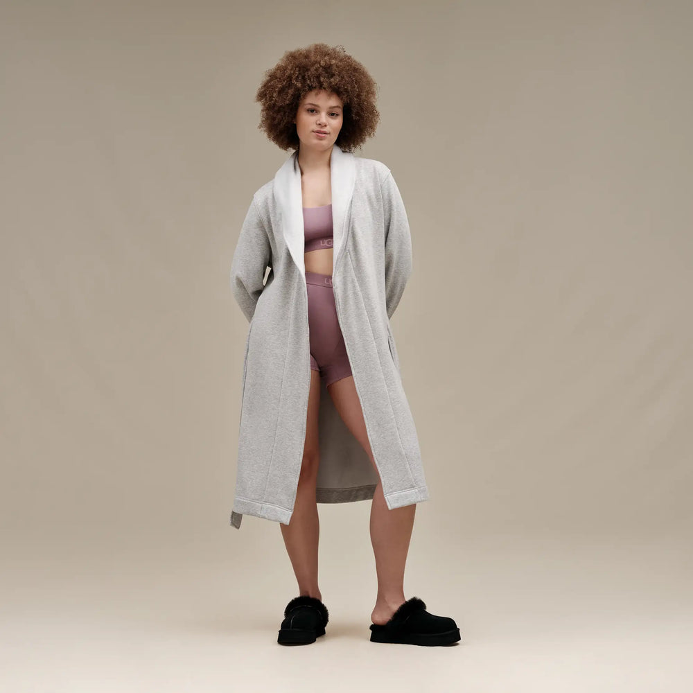 Woman wearing a long gray cardigan over a purple outfit on a beige background