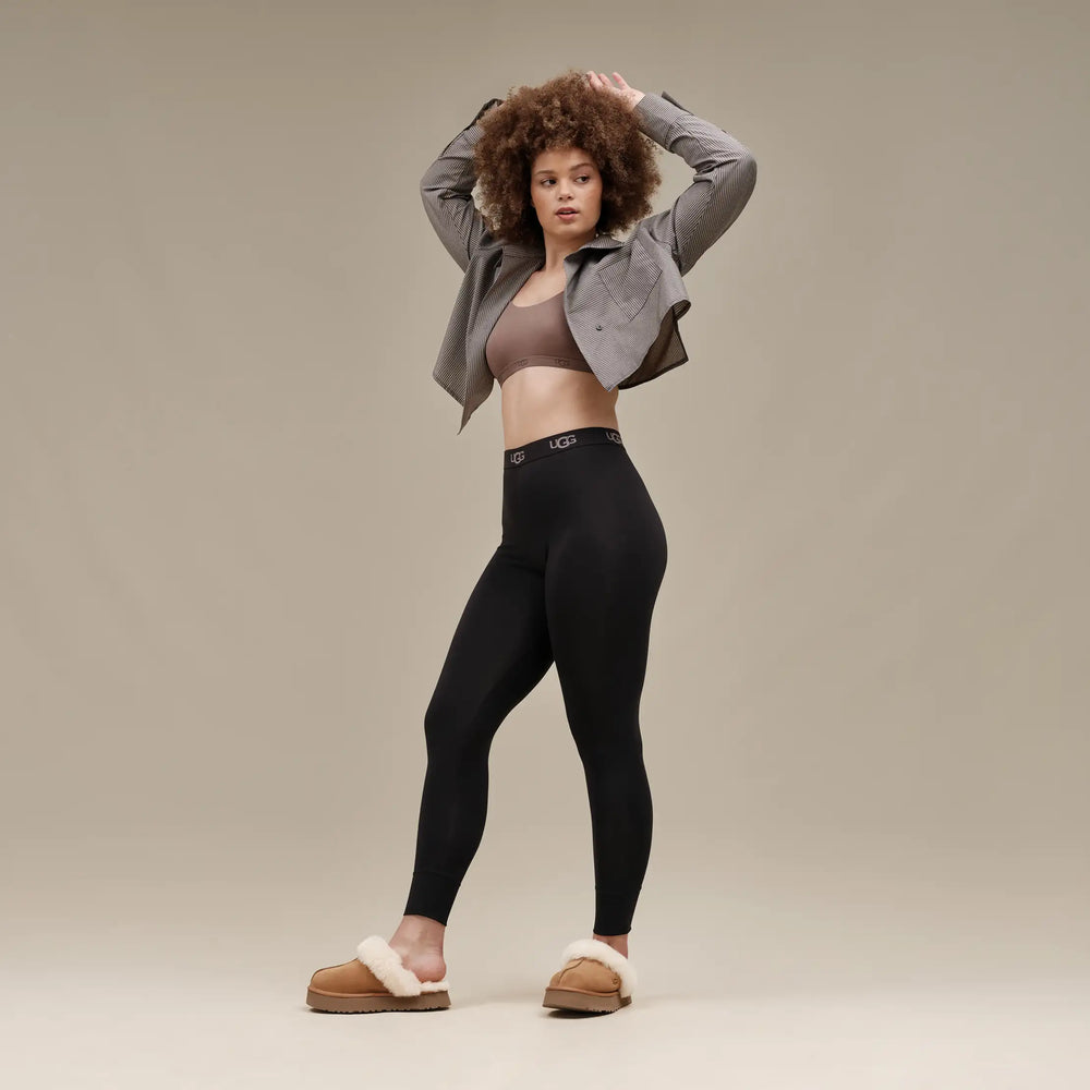 Woman wearing black leggings and a gray jacket on a beige background