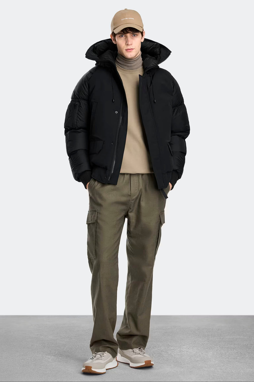 Man wearing a black jacket, beige cap, beige sweater, Canada Goose Paradigm Chilliwack Bomber Unisex Down Jacket at Volonka store.