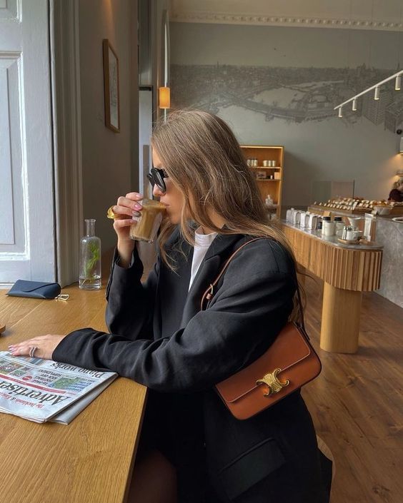 Woman drinking from a glass in a cafe with a Celine Triomphe Shoulder Bag at Volonka.