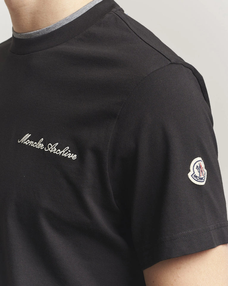 Moncler Men Signature Logo Tshirt displayed in black, featuring logo detail and contrasting neckline.