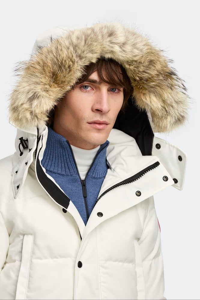 Man wearing a white winter coat with a fur-lined hood. Canada Goose Wyndham Parka Goose Men's Winter Jacket