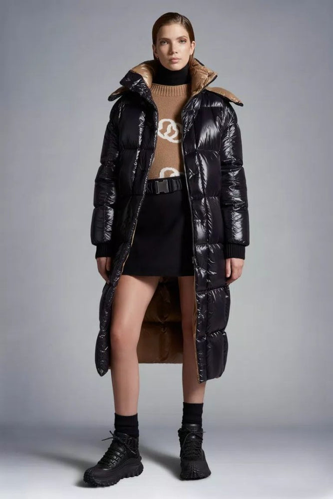 Woman wearing a long black puffer coat over a brown sweater and skirt. Moncler Cavettaz Hooded Long Down Jacket at volonka