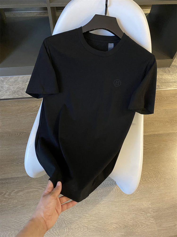 Black t-shirt on a mannequin with a logo, held by a hand on a wooden floor.