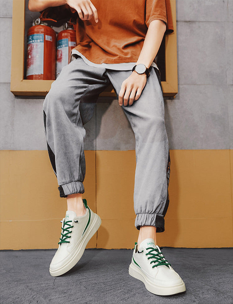 Person wearing gray jogger pants and white sneakers with green laces, sitting against a wall.