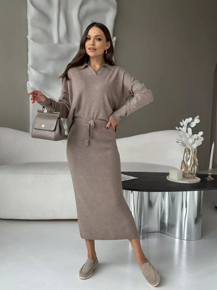 Woman in a beige outfit standing in a modern interior setting.