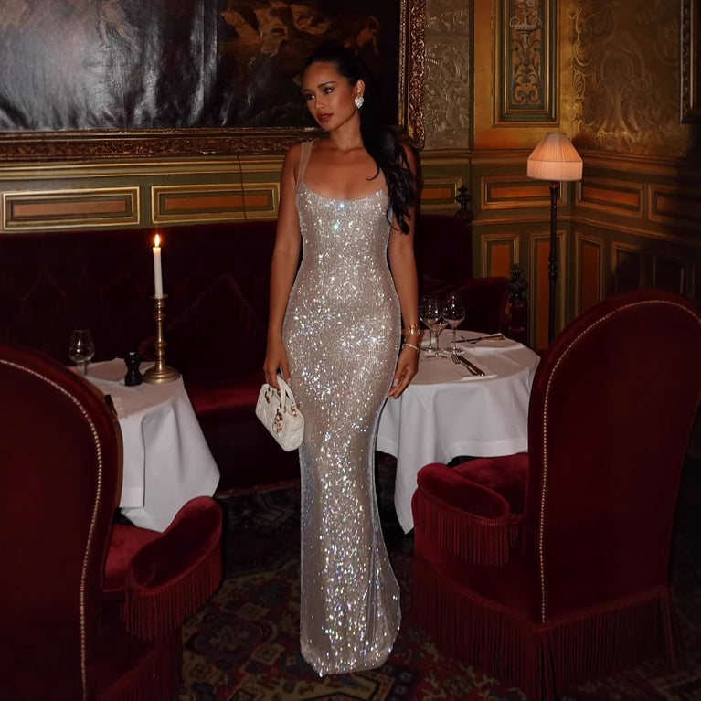 Model wearing a backless sparkly silver maxi evening dress in an elegant dining setting.