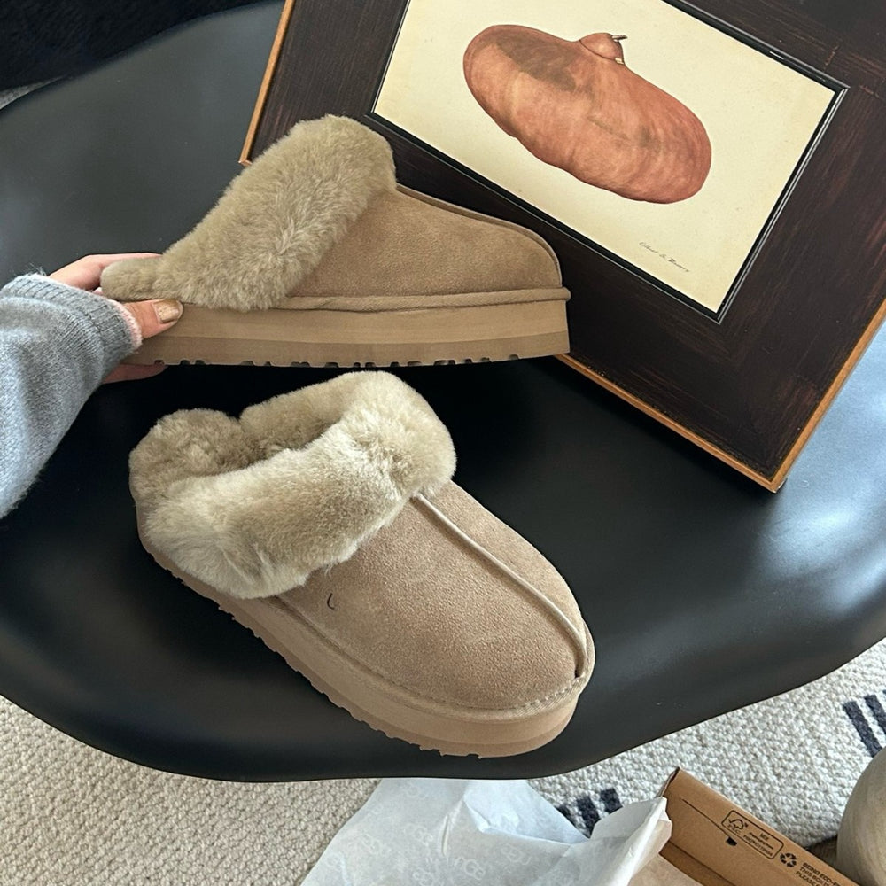Beige slippers on a black surface with a framed picture in the background