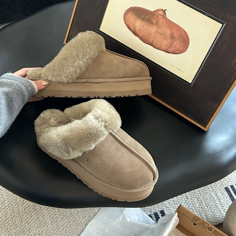 Beige slippers on a black surface with a framed picture in the background