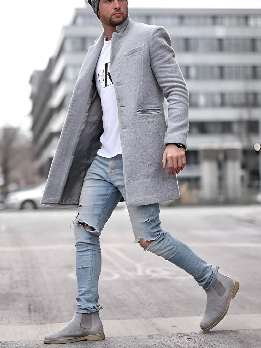 Man wearing a gray overcoat, white shirt, ripped jeans, and gray boots walking on a street.