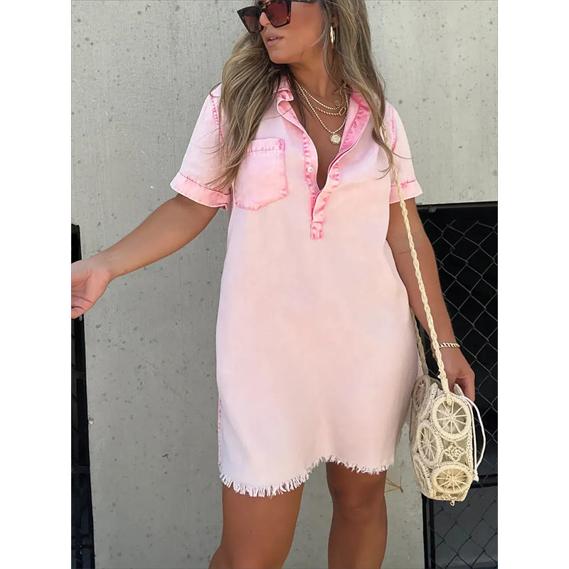 Woman wearing a pink and white denim dress with sunglasses and a handbag against a concrete wall.