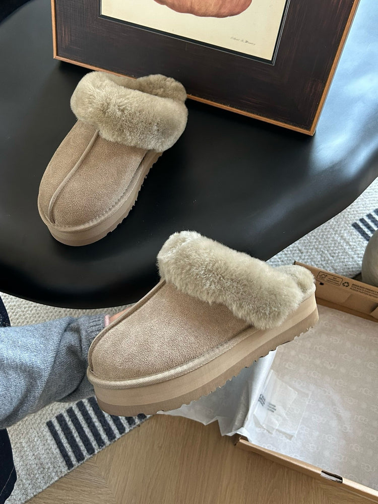 Pair of beige slippers with fur trim on a black surface.