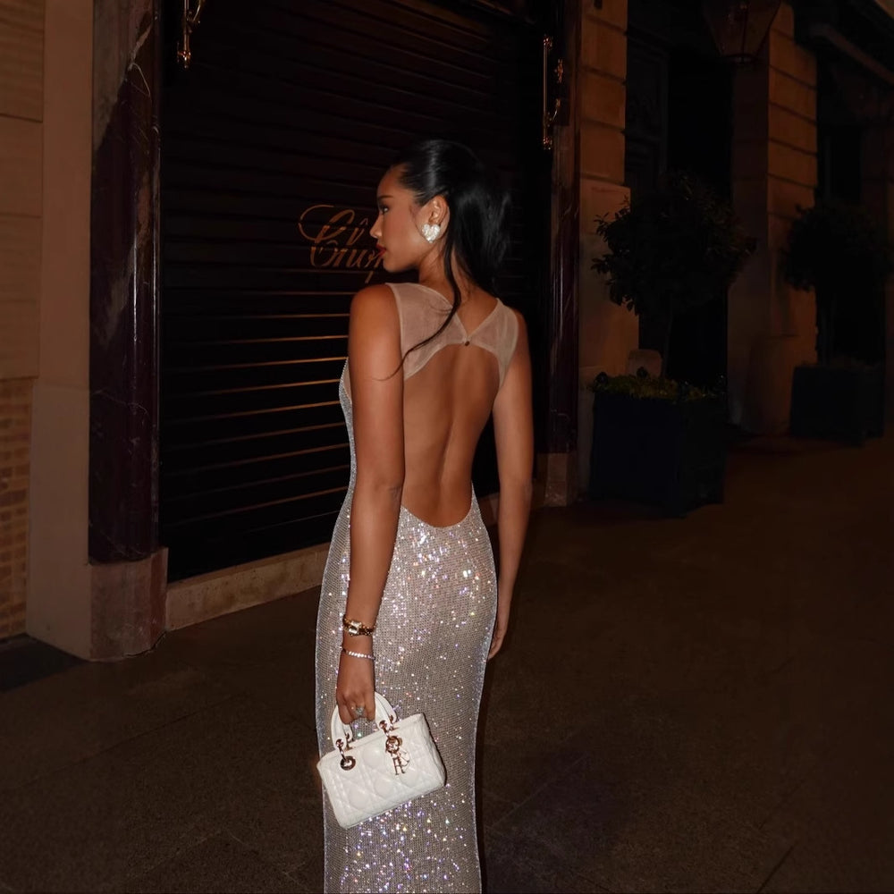 Elegant woman wearing a backless sparkly evening dress, showcasing a dazzling design and stylish handbag.