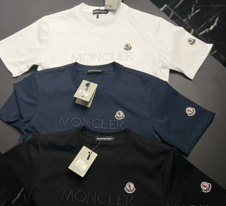 Three Moncler t-shirts in white, navy, and black on a dark surface.