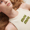 Close-up of a woman wearing a cream-colored sleeveless top with green MIUMIU premium stylish ribbed jersey top