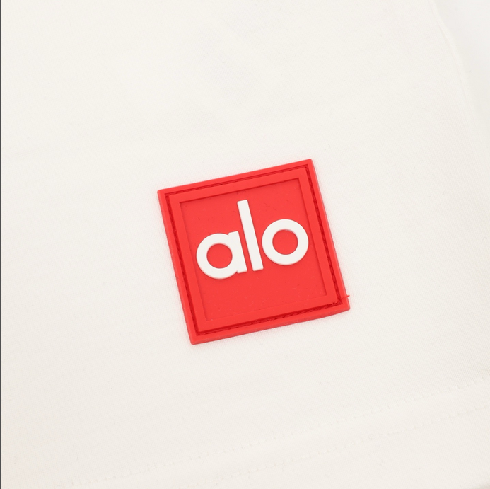 ALO Classic Minimal Short Sleeve Tshirt in white with logo on chest and red tag detail.