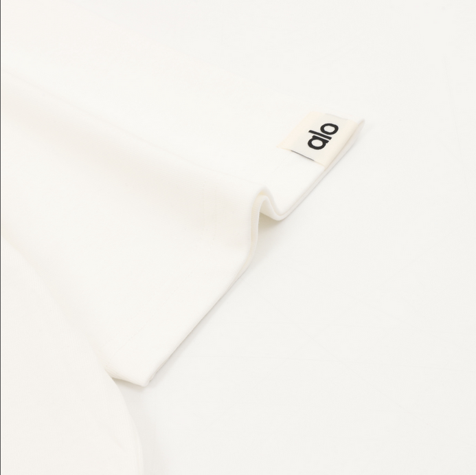 ALO Classic Minimal Short Sleeve Tshirt in white with logo on chest and red tag detail.