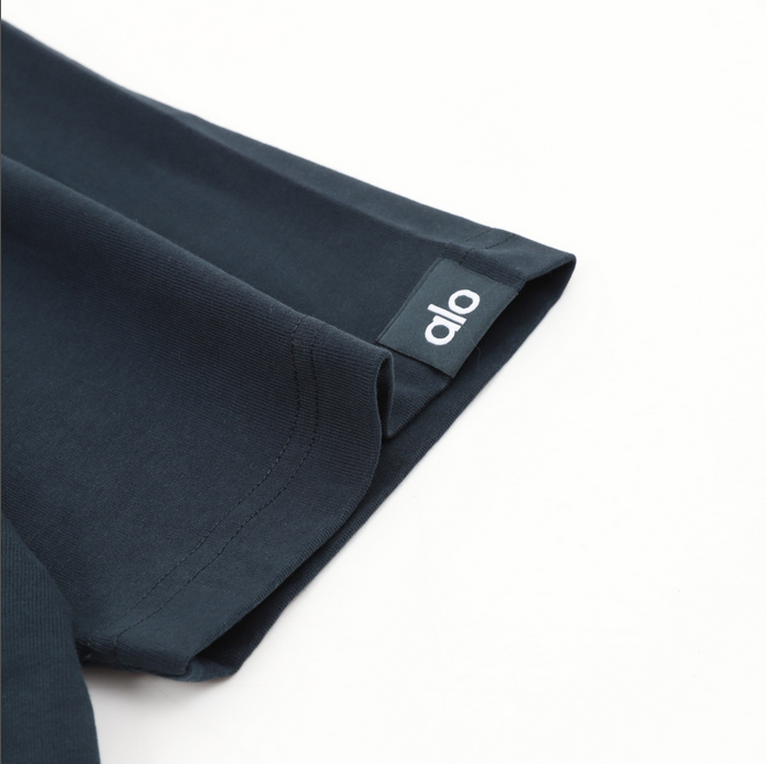 ALO Classic Minimal Short Sleeve Tshirt in navy blue with logo on chest and red tag detail.