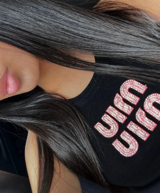 woman wearing a black hoodie with pink text, close-up of face and hoodie. MIUMIU premium stylish ribbed jersey top