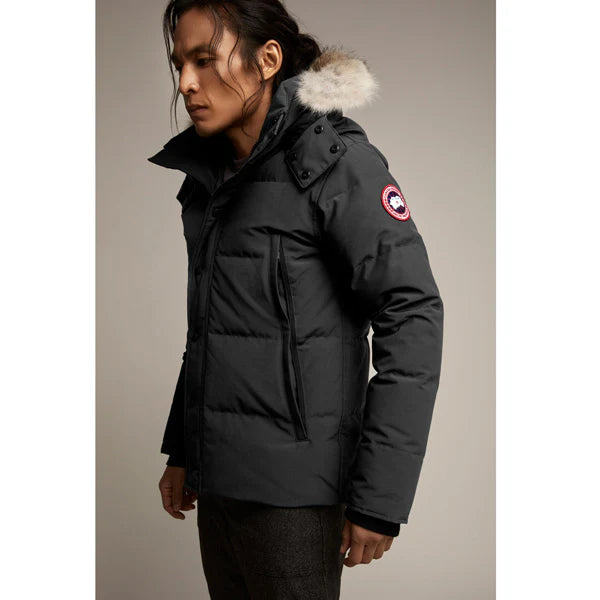Man wearing a dark black puffer jacket with a fur-lined hood. Canada Goose Wyndham Parka Goose Men's Winter Jacket at Volonka.