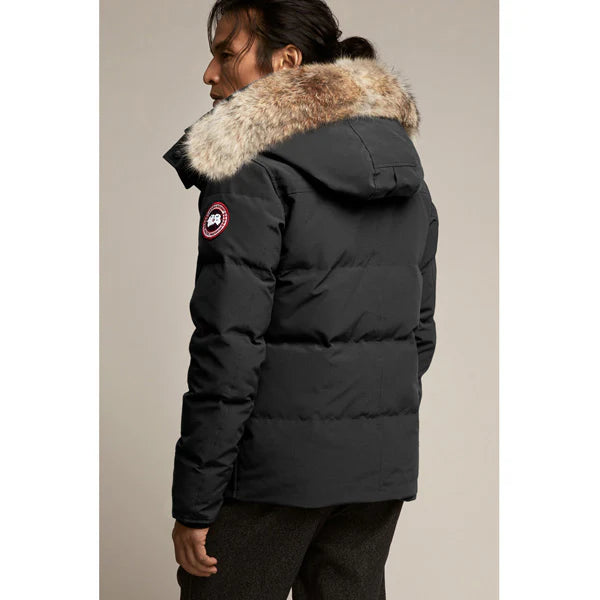 Canada Goose Wyndham Parka Goose Men's Winter Jacket at Volonka. Man wearing a black puffer jacket with fur hood on a beige background