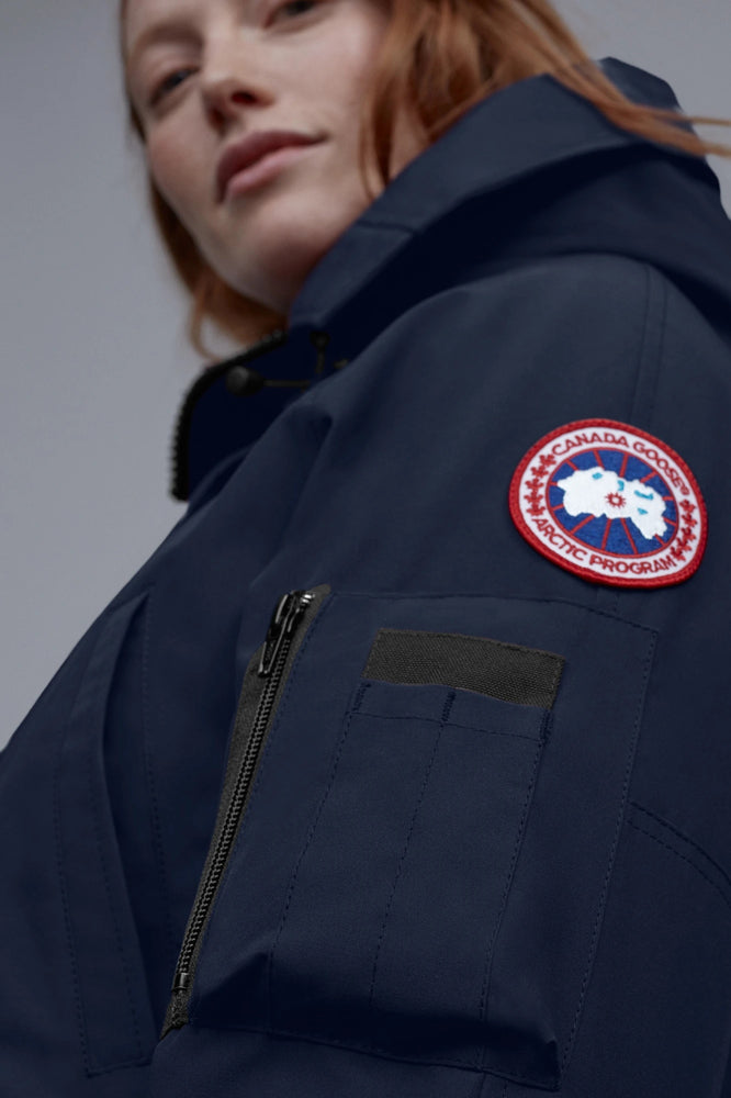 Person wearing a navy blue jacket with a Canada Goose logo on a gray background
