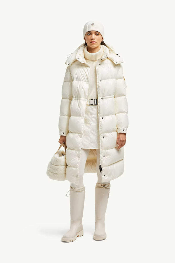 Person wearing a long white puffer coat with a matching hat and boots. Moncler Cavettaz Hooded Long Down Jacket