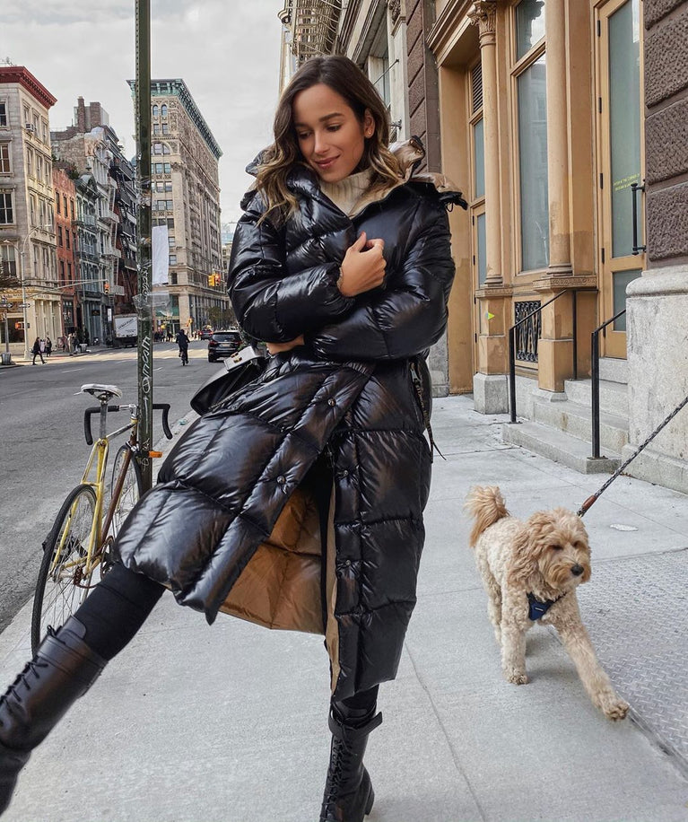 Woman in a black puffer coat walking a dog on a city street. Moncler Cavettaz Hooded Long Down Jacket