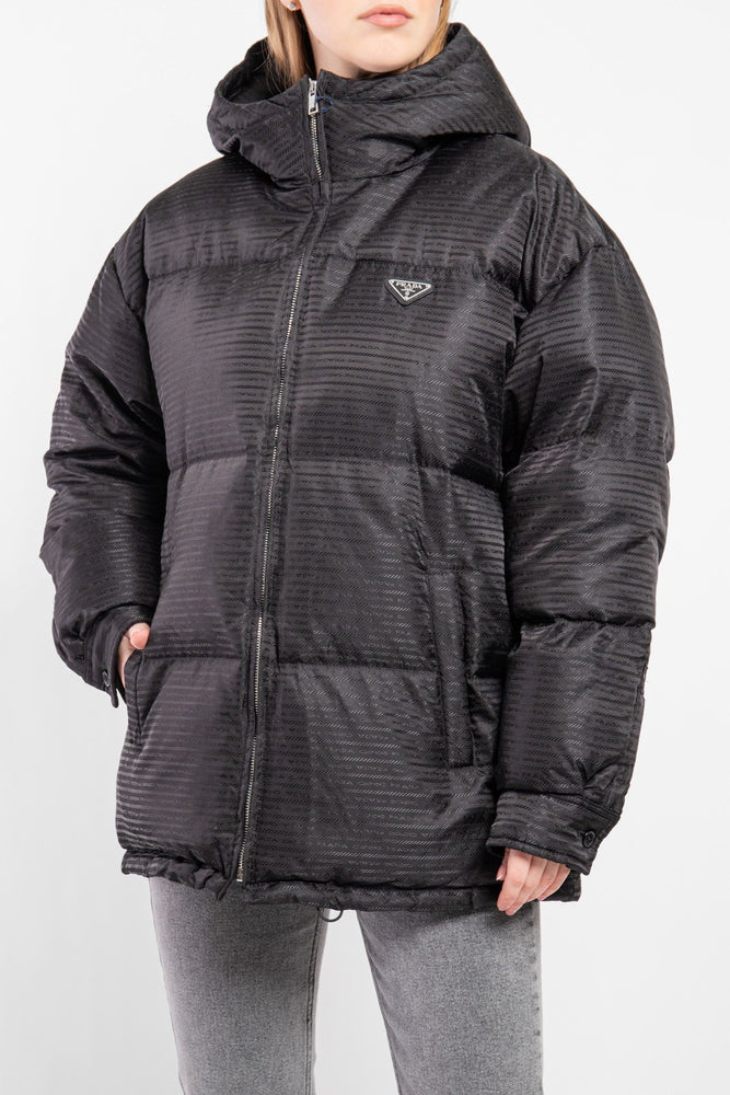 Woman wearing a black puffer jacket with a brand logo. Prada Puffer Down Jacket Unisex