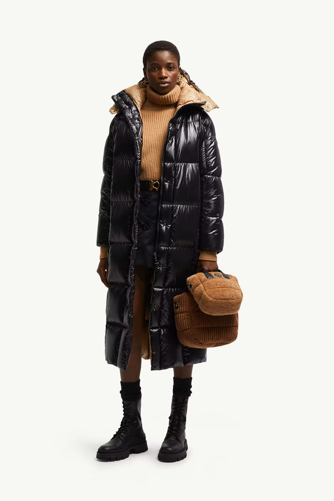 Person wearing a black puffer coat with a hood, holding a brown bag on a white background