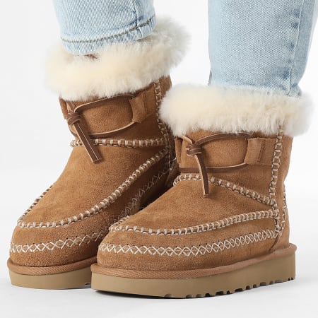 Brown UGG boots with white fur lining worn with light blue jeans on a white background