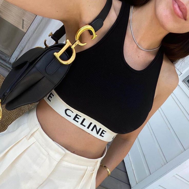 woman wearing a black crop top and white shorts with 'CELINE' branding, holding a black bag with a gold clasp in volonka store