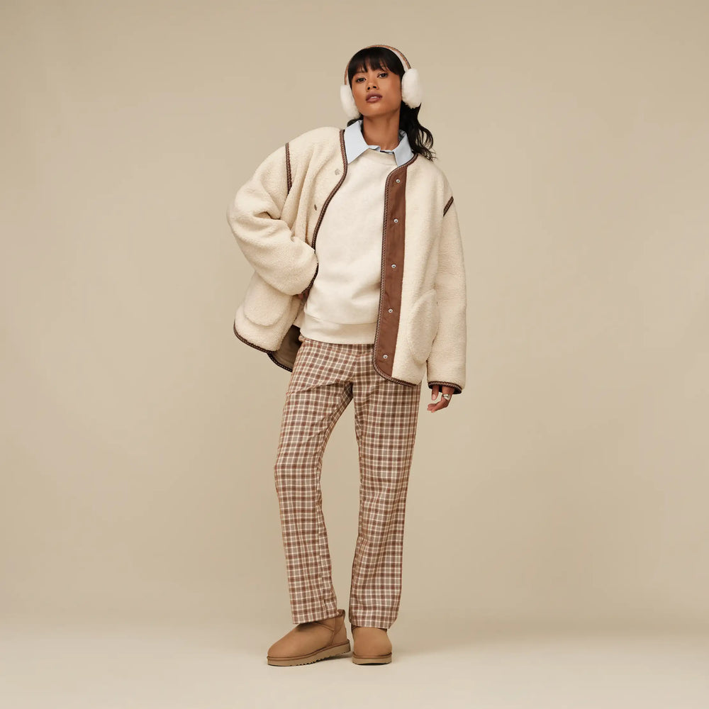 woman wearing a cream jacket with brown accents, plaid pants, and beige boots on a beige background.