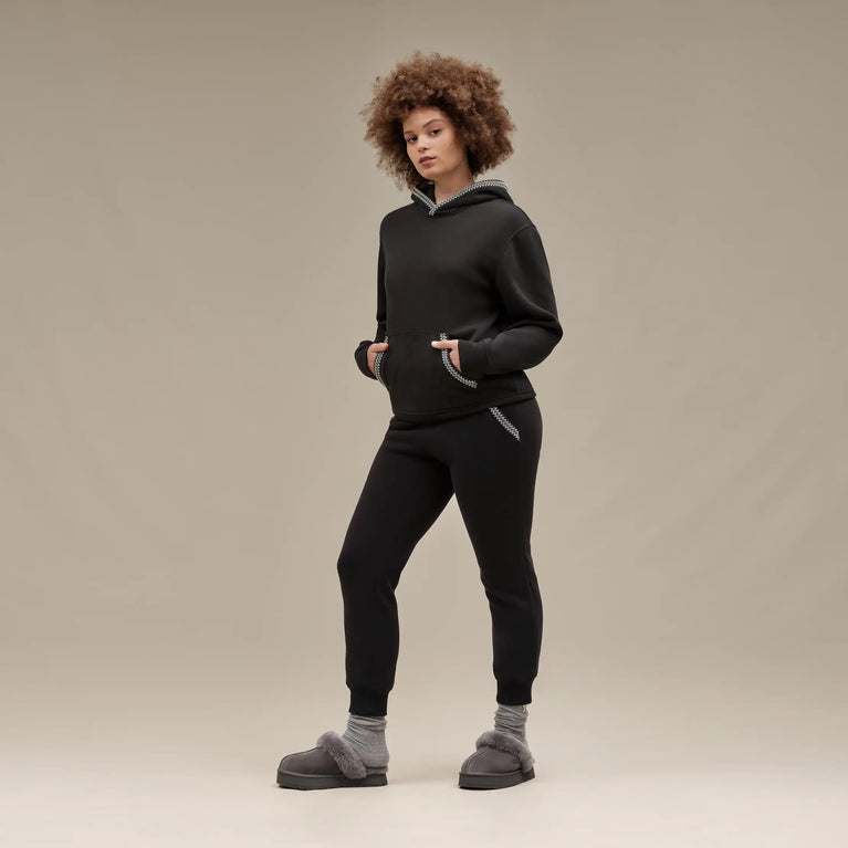 Person wearing a black hoodie and pants with gray slippers on a beige background