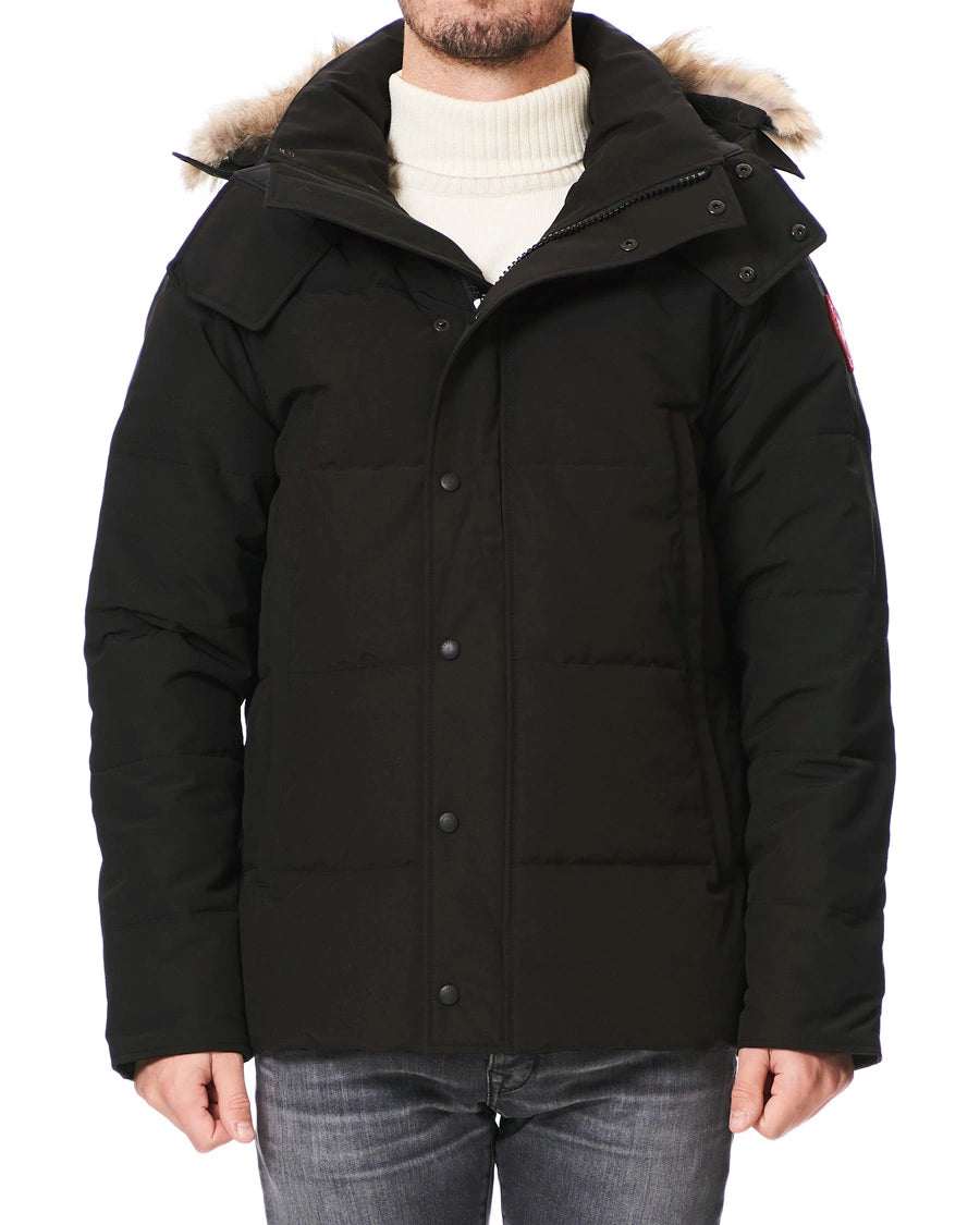 Black winter jacket with fur-lined hood worn by a person on a white background. Canada Goose Wyndham Parka with Fur jacket.