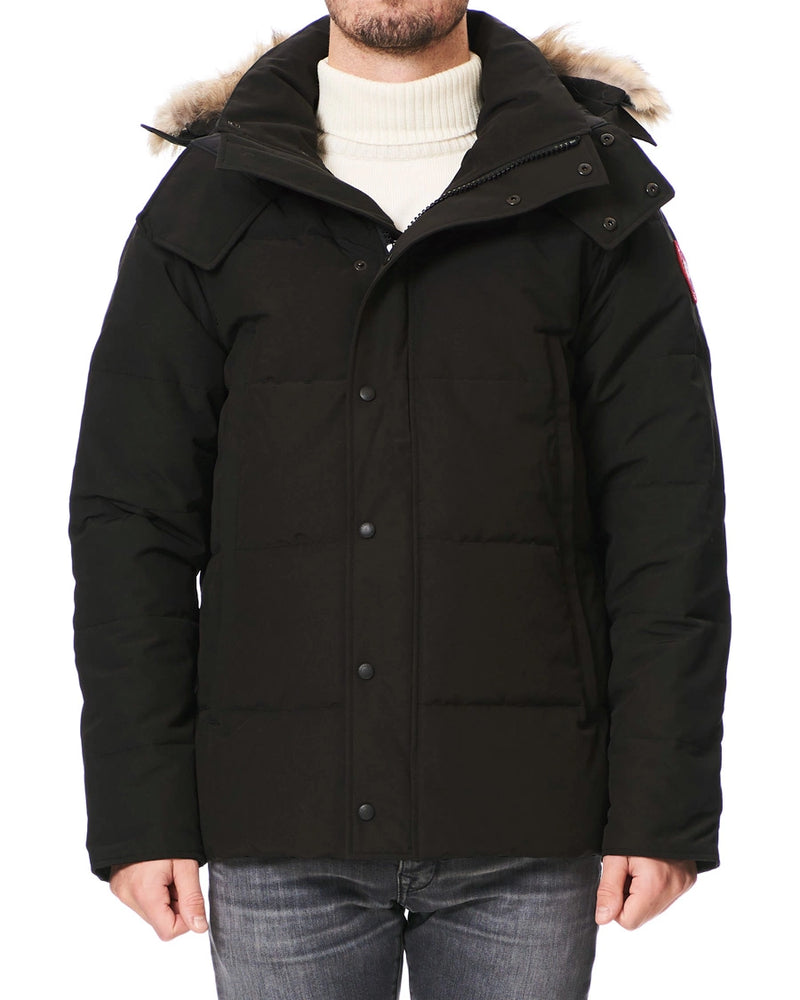 Black winter jacket with fur-lined hood worn by a person on a white background. Canada Goose Wyndham Parka with Fur jacket.