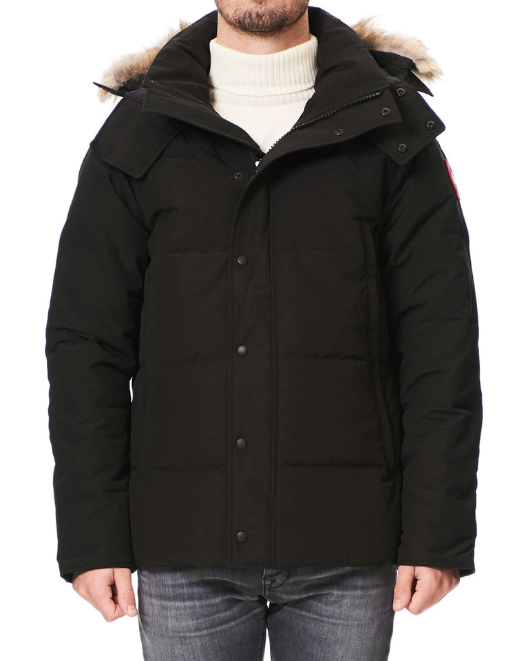 Black winter jacket with fur-lined hood worn by a person on a white background. Canada Goose Wyndham Parka with Fur jacket.