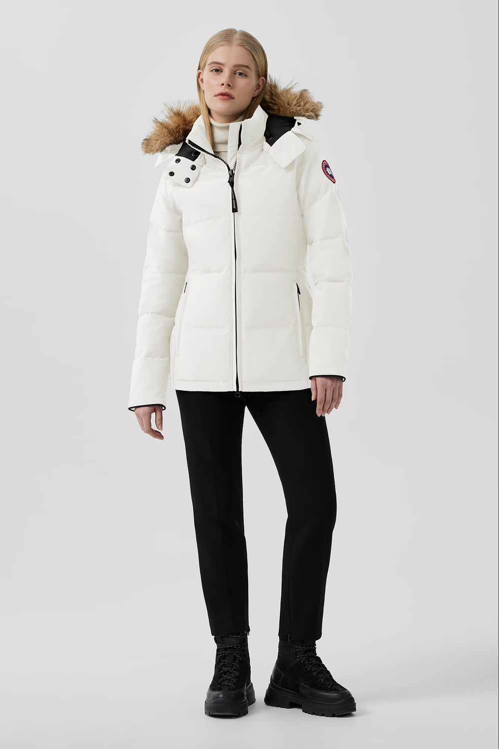 Woman wearing Canada Goose Chelsea Parka Women's Down Winter Jacket at Volonka store. White winter coat with fur hood on a light gray background