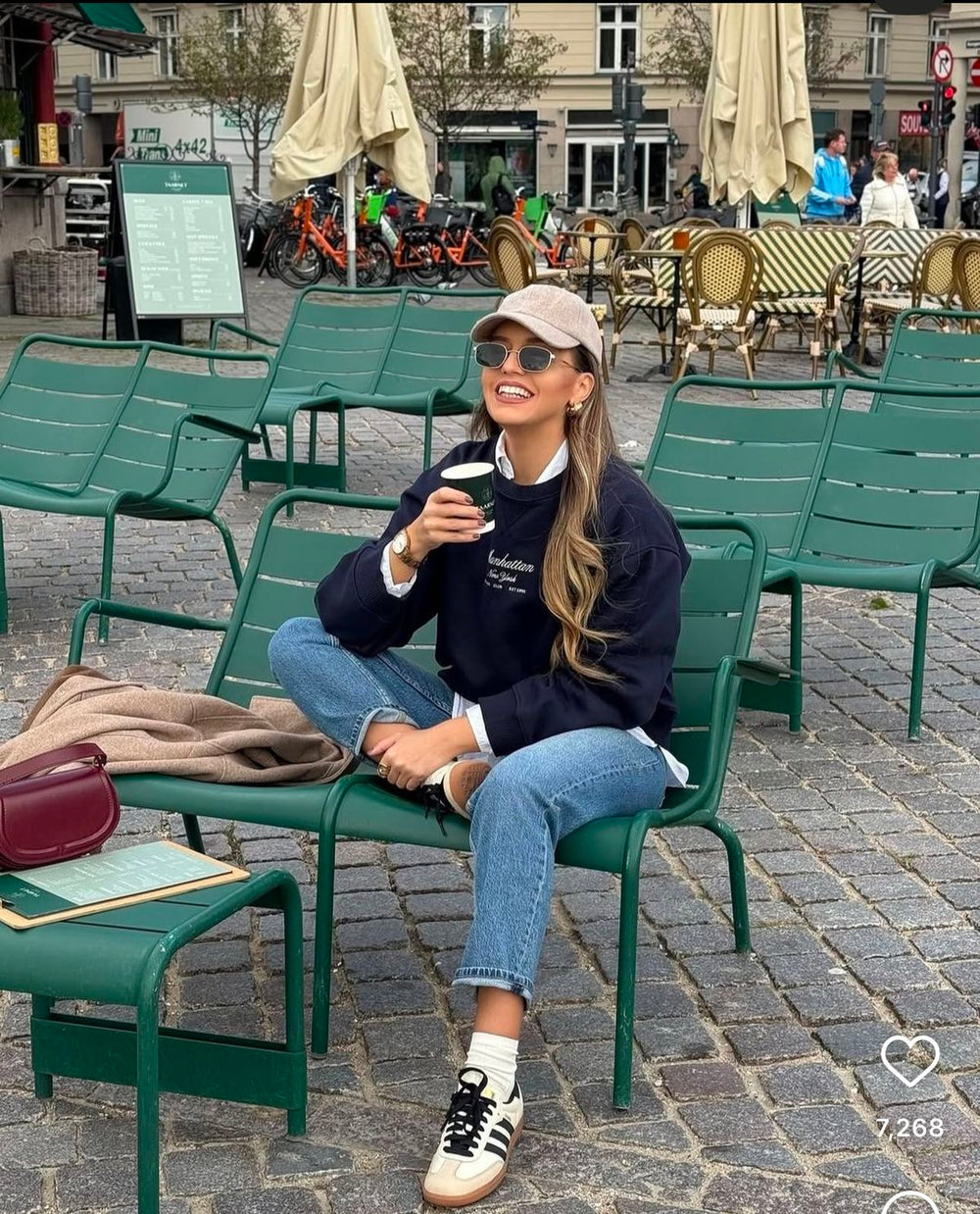 Woman sitting on a green chair wearing Adidas Samba OG Cream White Sneaker, enjoying a drink outdoors.