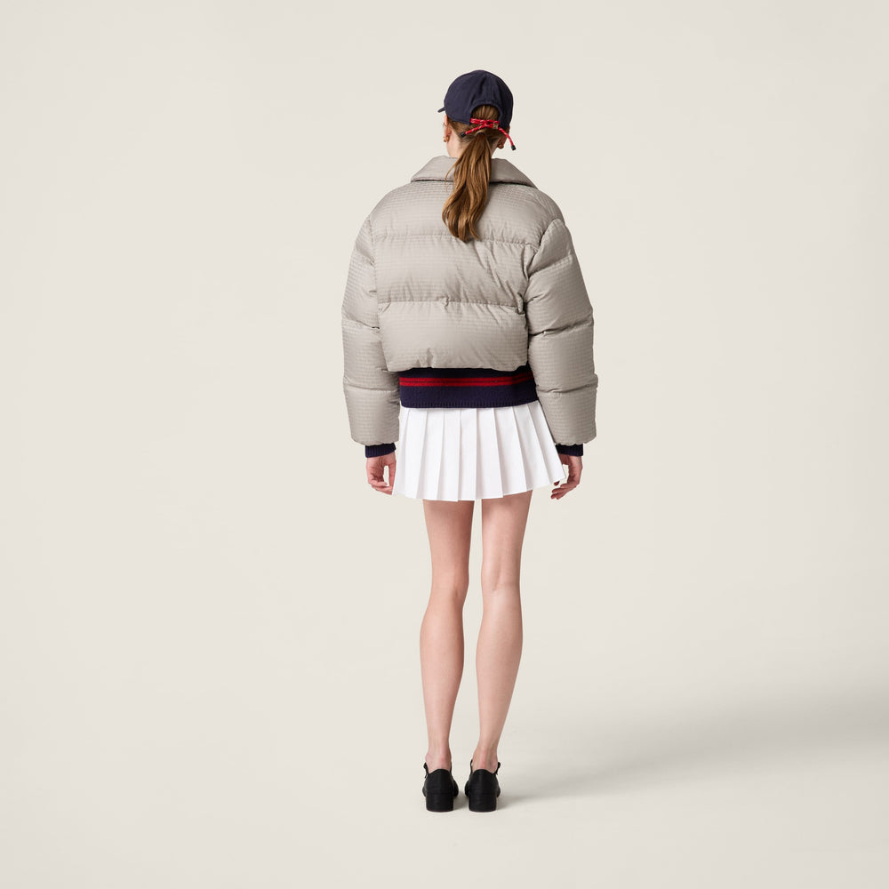 Person wearing a MIUMIU light gray puffer jacket and white skirt on a plain background