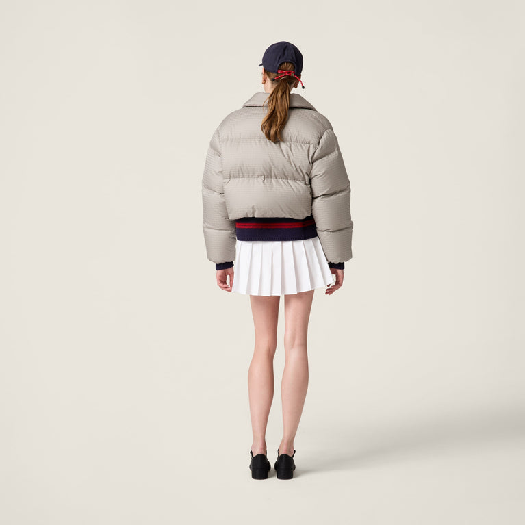 Person wearing a MIUMIU light gray puffer jacket and white skirt on a plain background