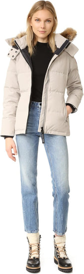 Woman wearing a beige puffer jacket with a fur-lined hood, black top, and blue jeans. Canada Goose Chelsea Parka Women's Down Winter Jacket at Volonka store.