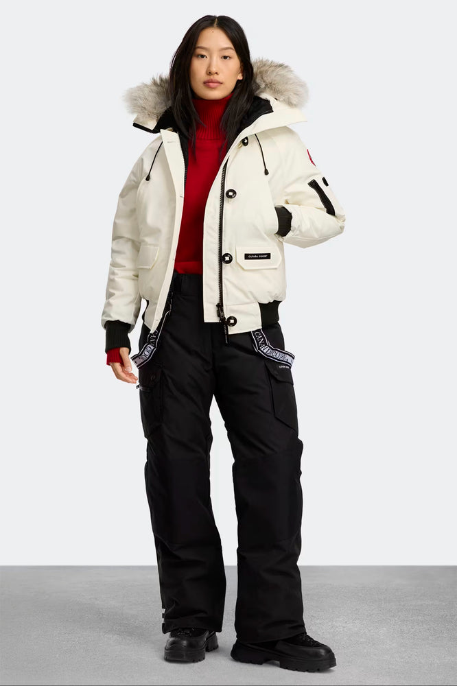 woman wearing a white winter jacket with fur hood and black pants on a light gray background