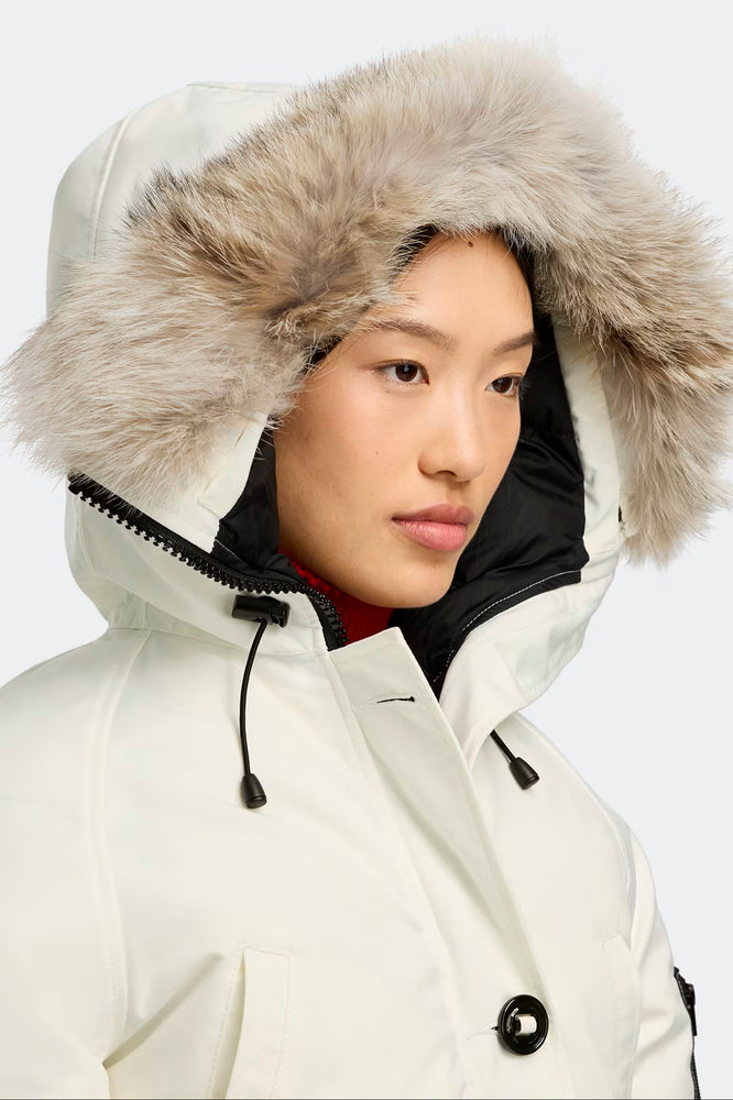Person wearing canada goose white parka with a fur-lined hood on a plain background