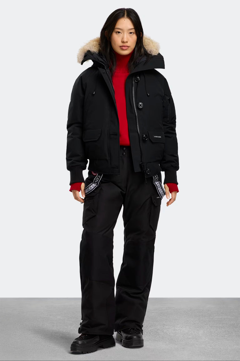 Person wearing a black winter coat with fur-lined hood and black pants on a white background