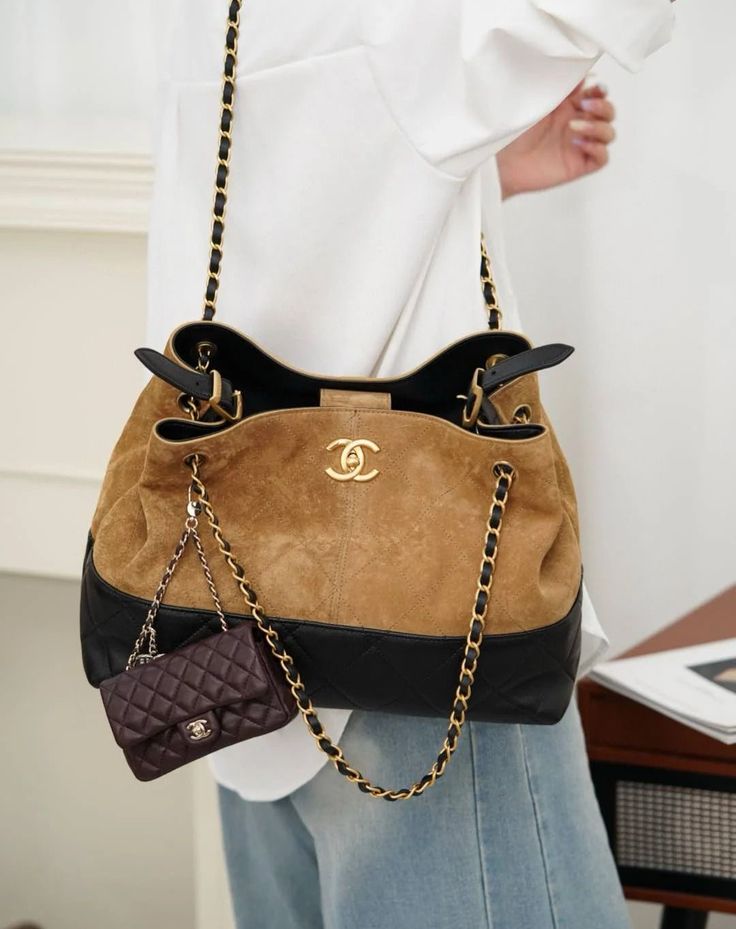 Brown and black handbag with gold chain strap held by a person wearing a white shirt and blue jeans.