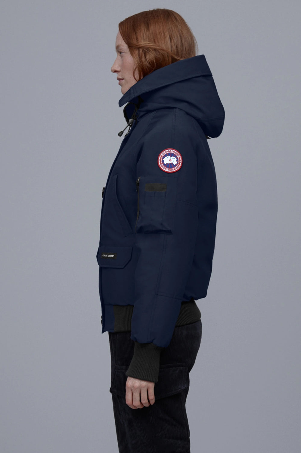 Person wearing a navy blue coat with a brand logo on a gray background. Canada Goose Chilliwack Bomber Women's Winter Hooded Jacket
