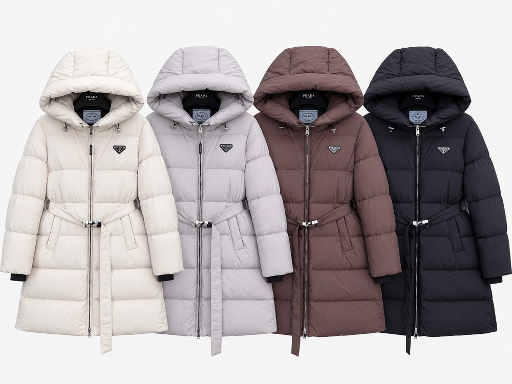 Four hooded puffer coats shown side by side on a light gray background, in cream, pale gray, taupe-brown, and black. Each coat has a front zipper, hood, tie belt, and a small triangular Prada logo on the chest.