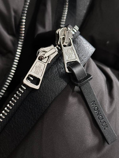 Close-up of a black Moncler bag with silver zippers and logo. Moncler Men's Besbre Padded Jacket